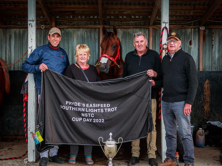 Four people pose with a winning horse and trophy under a stable roof on Cup Day 2022 at the Pryde&rsquo;s EasiFeed Southern Lights Trot