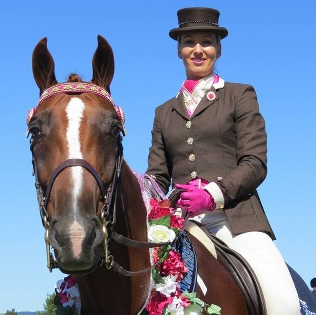 Rider in a brown habit and top hat alongside a chestnut Standardbred in a floral garland